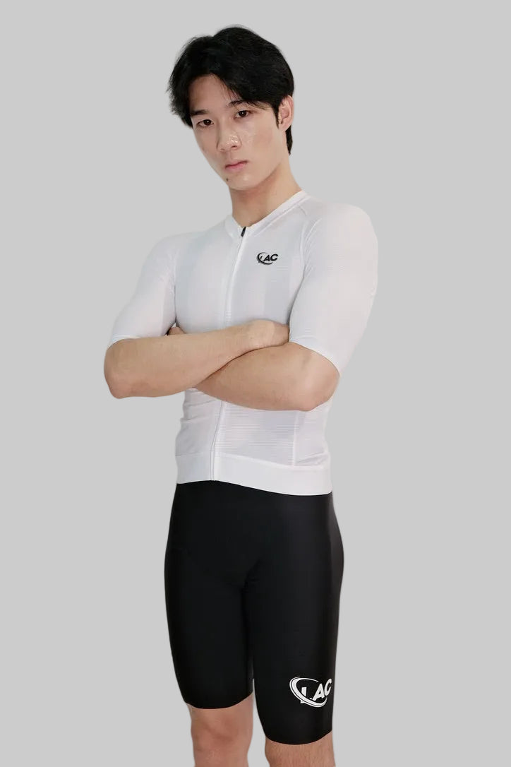 Person wearing a white cycling jersey and black shorts with a logo on a light gray background