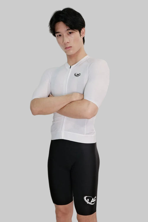 Person wearing a white cycling jersey and black shorts with a logo on a light gray background