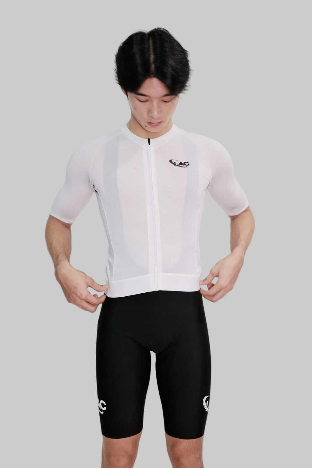 Person wearing a white cycling jersey and black shorts with a visible brand logo on a white background