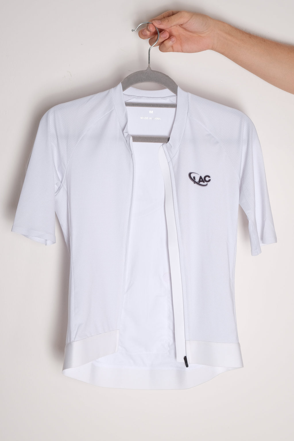 White cycling jersey with a brand logo held by a hand on a light background